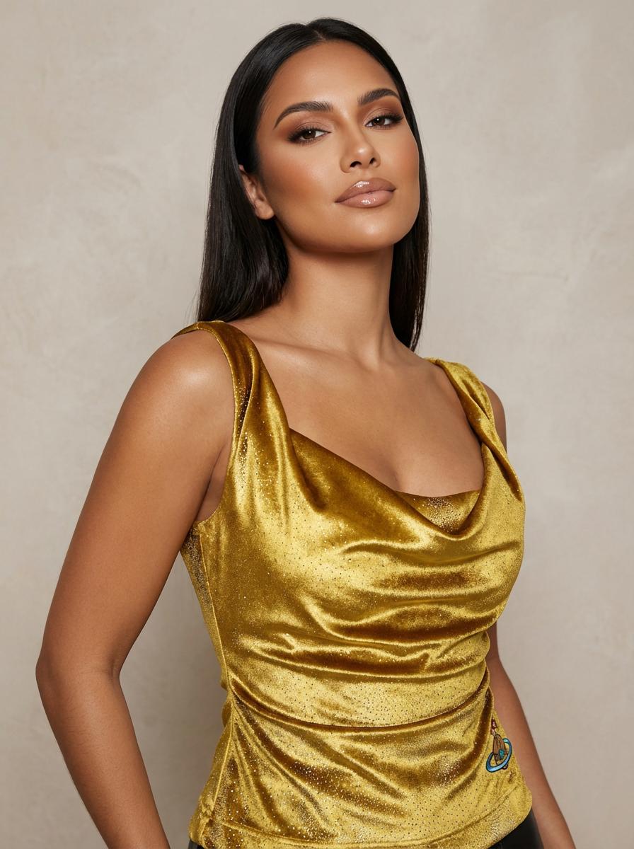 A Woman Stands Against A Neutral Background Wearing A Shimmering Gold Top Paired With Sleek Black Pants before