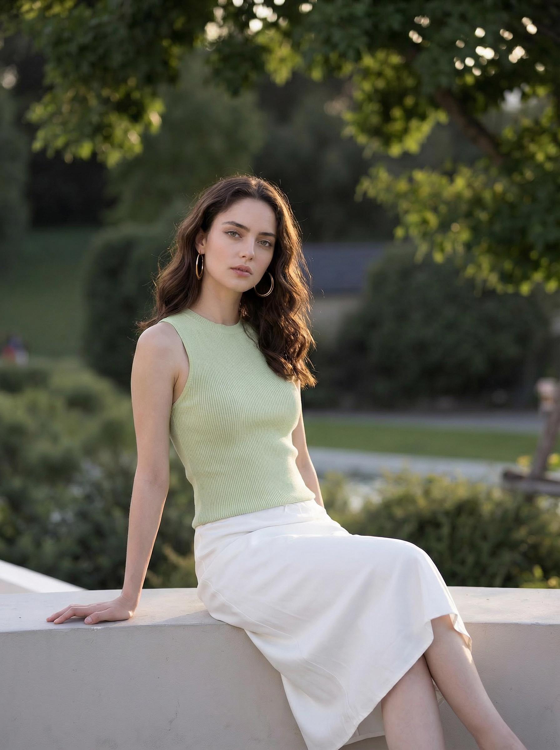 A Woman Is Seated Outdoors On A Concrete Ledge Surrounded By Lush Greenery Under The Soft Glow Of Sunlight